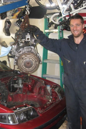 A man lifting an engine out of a car on an engine hoist
